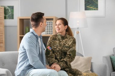 Woman in military uniform with her husband on sofa at home clipart