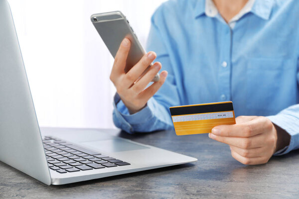 Young woman with credit card using smartphone at table