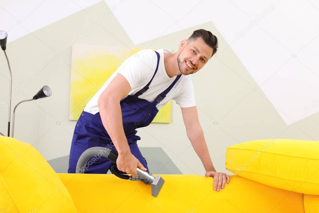 Dry cleaning worker removing dirt from sofa indoors
