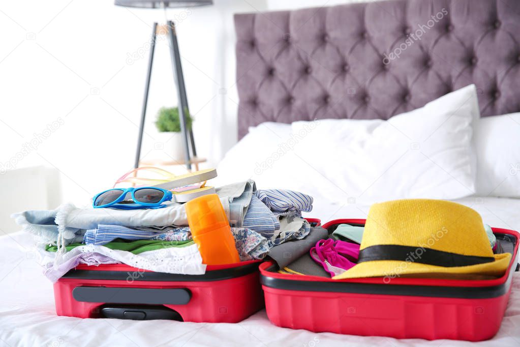 Open suitcase with different clothes and accessories for summer journey on bed
