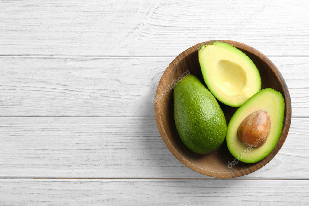 Bowl with ripe avocados on wooden background, top view