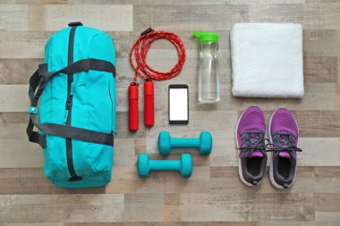 Flat lay composition with sports bag and gym equipment on wooden floor, top view clipart