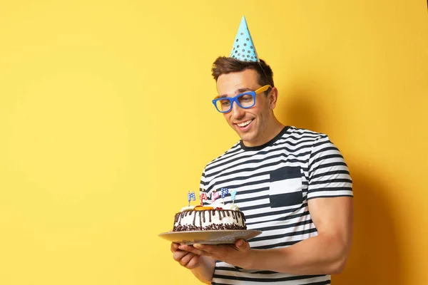 Young man with birthday cake on color background