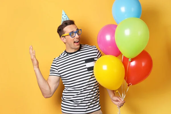 Young man with bright balloons on color background. Birthday celebration