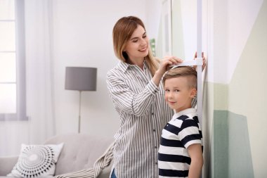 Young woman measuring her son's height at home clipart