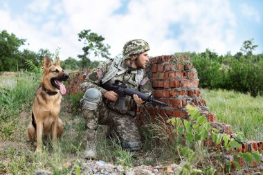 Atış poligonunda Alman çoban köpeği olan askeri üniformalı bir adam.