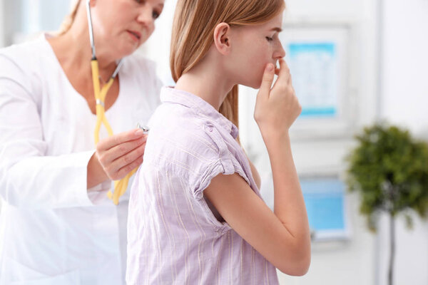 Doctor examining coughing teenage girl at clinic