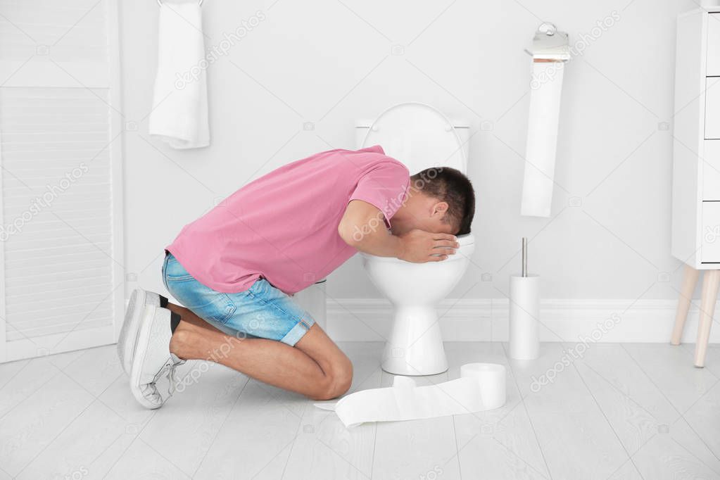 Young man vomiting in toilet bowl at home