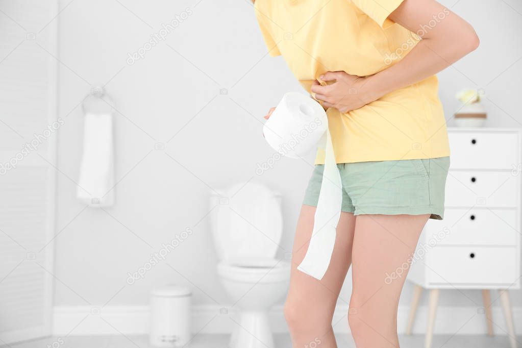 Young woman with bath tissue standing near toilet bowl at home