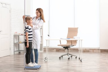 Doctor measuring little boy's height in hospital clipart