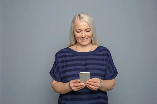 灰色の背景に携帯電話を使用しての成熟した女性 — ストック写真
