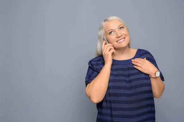 Rijpe Vrouw Praten Mobiele Telefoon Tegen Een Grijze Achtergrond — Stockfoto