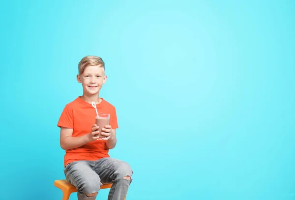 小男孩与玻璃牛奶震动在凳子反对颜色背景 — 图库照片