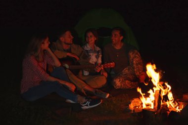 Genç adam gece şenlik ateşi arkadaşları için gitar çalmak. Kamp sezon