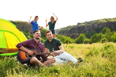 Bir grup genç insan bira ve gitar kamp çadır içinde ekilmemiş boş arazi yakın dinlenme