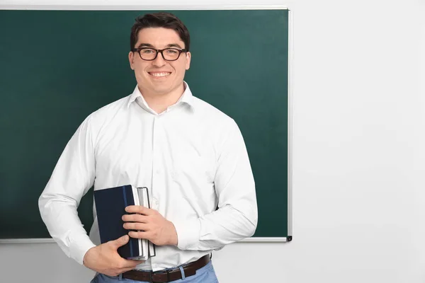 Portrait of male teacher with notebooks near chalkboard in classroom