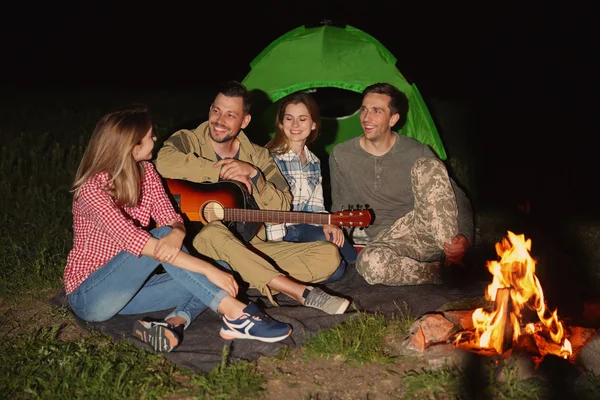 Genç adam gece şenlik ateşi arkadaşları için gitar çalmak. Kamp sezon