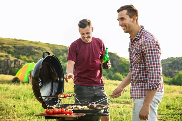 Young people having barbecue in wilderness. Camping season