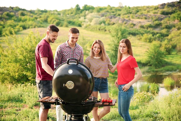 Young people having barbecue in wilderness. Camping season