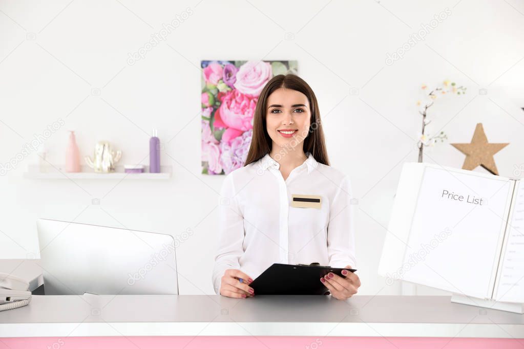 Young receptionist with clipboard at desk in beauty salon
