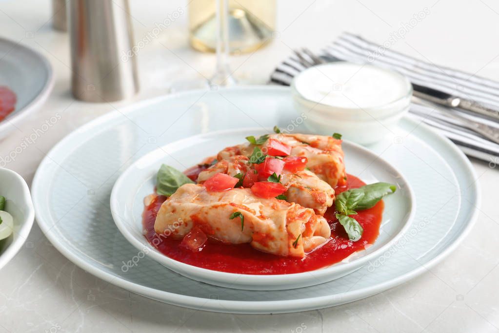 Plate with stuffed cabbage leaves in tomato sauce on table