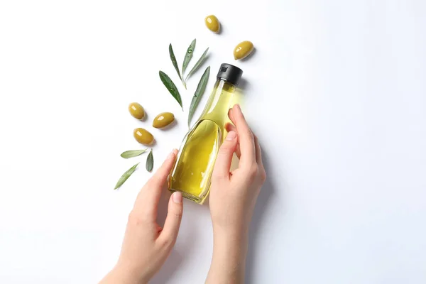 Woman holding bottle with oil and ripe olives on white background