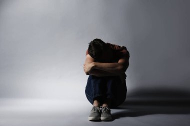 Gri arka plan üzerinde oturan yalnız depresif adam