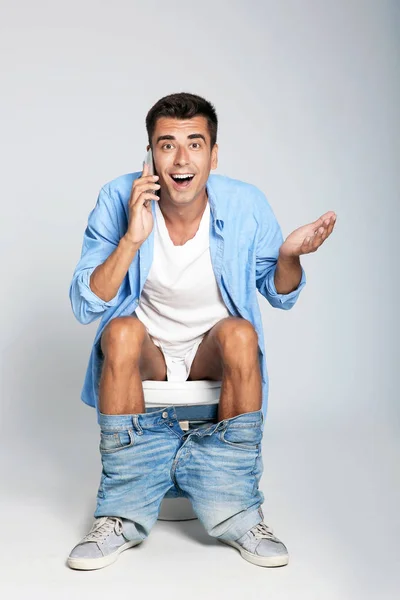 Hombre Joven Con Teléfono Móvil Sentado Inodoro Sobre Fondo Gris — Foto de Stock