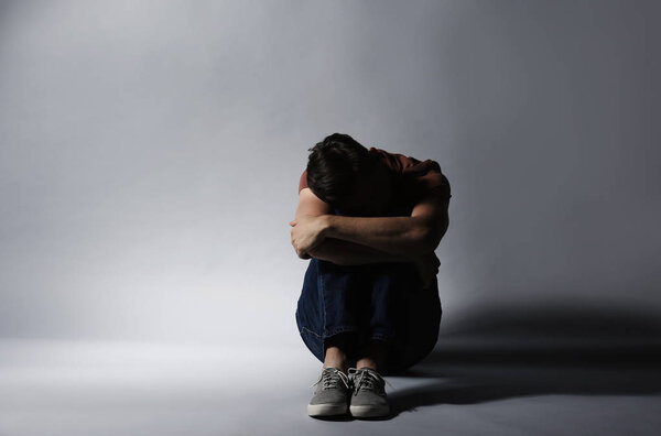 Одинокий депрессивный мужчина сидит на сером фоне
