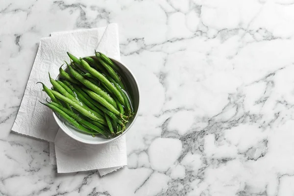 stock image Bowl with fresh green French beans and water on marble table, top view