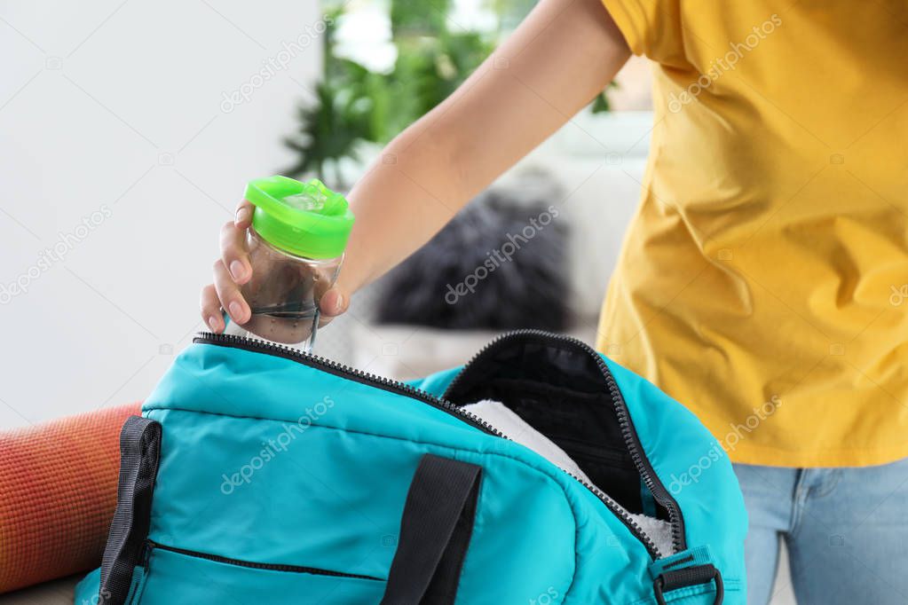 Young woman packing sports bag at home