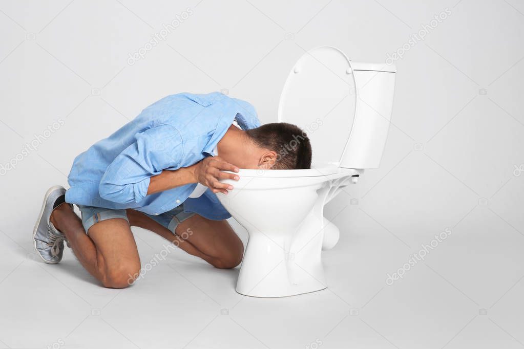 Young man vomiting in toilet bowl on gray background