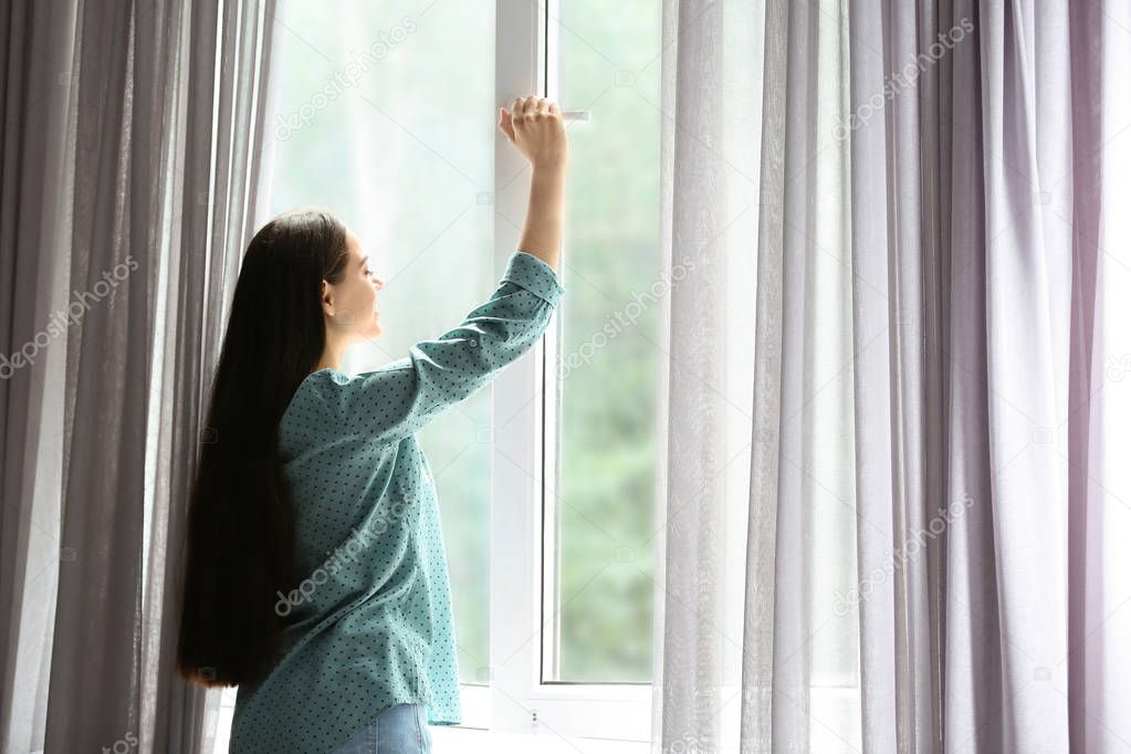 Young beautiful woman opening big window in room