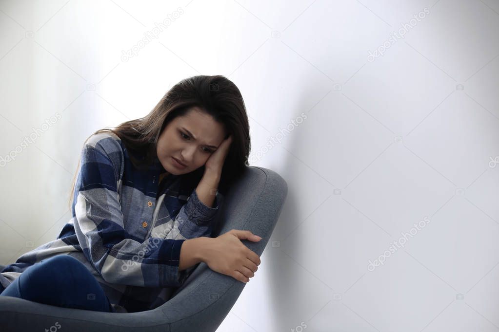 Depressed young woman in armchair near light wall