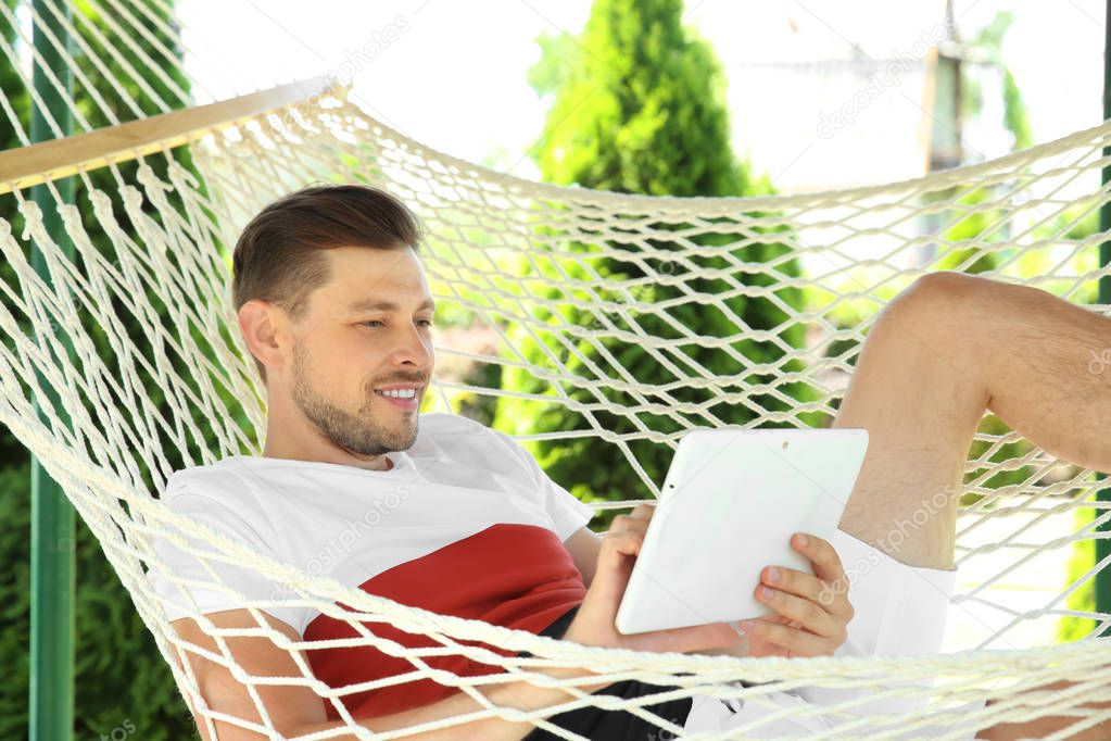 Man with tablet relaxing in hammock outdoors on warm summer day