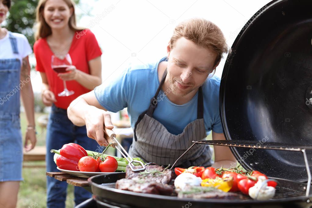 Man cooking meat and vegetables on barbecue grill outdoors