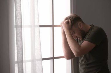 Depresyondaki genç adam evinin penceresinin yanında.