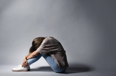 Gri arka plan üzerinde oturan yalnız depresif kadın