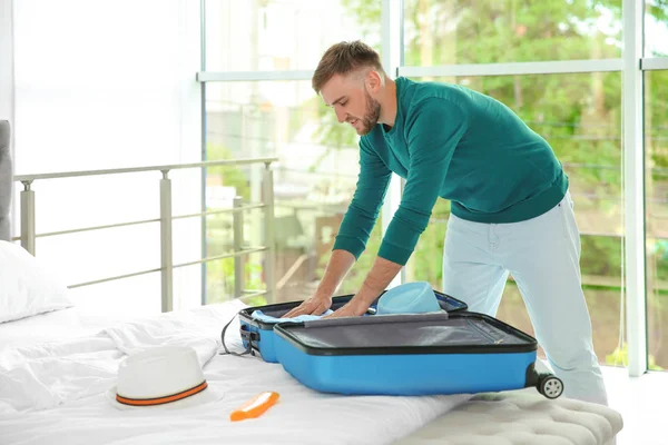 Young man packing suitcase for summer journey on bed