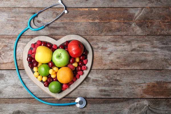 Herzförmiger Teller Mit Frischen Früchten Und Stethoskop Auf Holztisch Draufsicht — Stockfoto