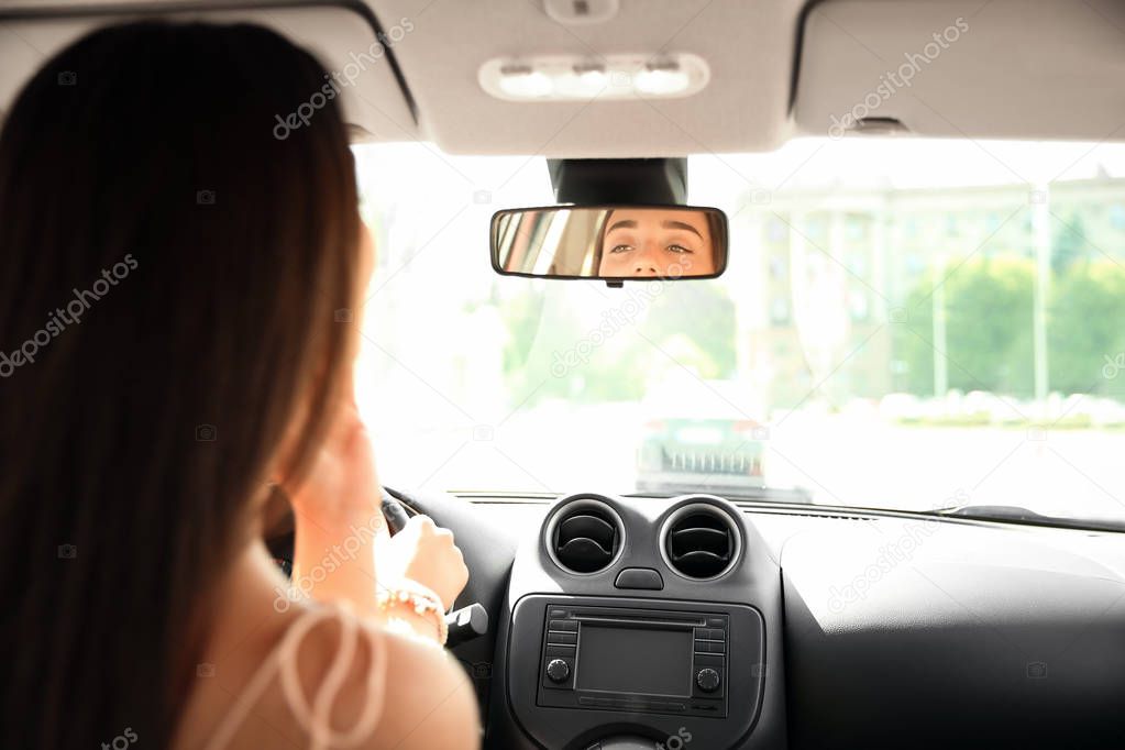 Young woman looking in rearview mirror of car