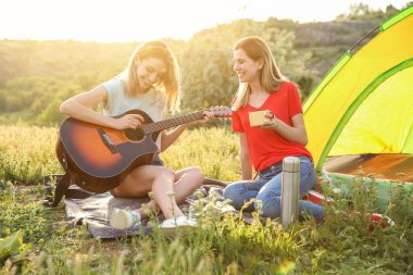 Genç kadın sıcak içecek ve kamp çadır içinde ekilmemiş boş arazi yakınındaki gitar ile dinlenme