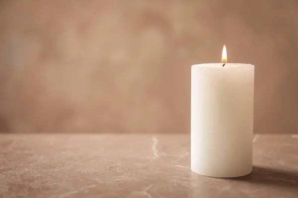 Beautiful burning wax candle on table against grey background