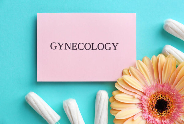 Card with word GYNECOLOGY, tampons and flower on color background, top view