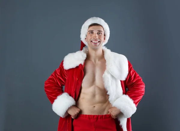 Young muscular man in Santa Claus costume  on gray background
