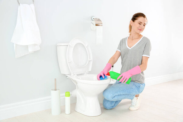 Женщина чистит унитаз в ванной комнате
