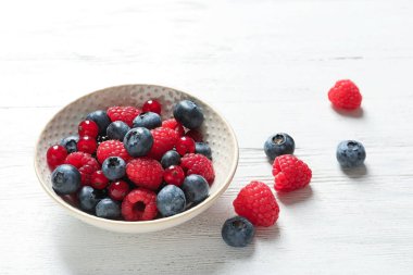 Frambuaz, frenk üzümü ve ahşap masa üzerinde yaban mersini ile kase