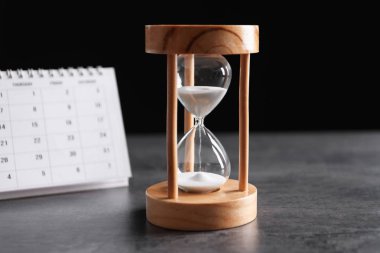 Hourglass and calendar on table against black background. Time management clipart