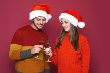 Genç çift Santa tungur bardak şampanya renk arka plan üzerinde şapka. Noel kutlamaları