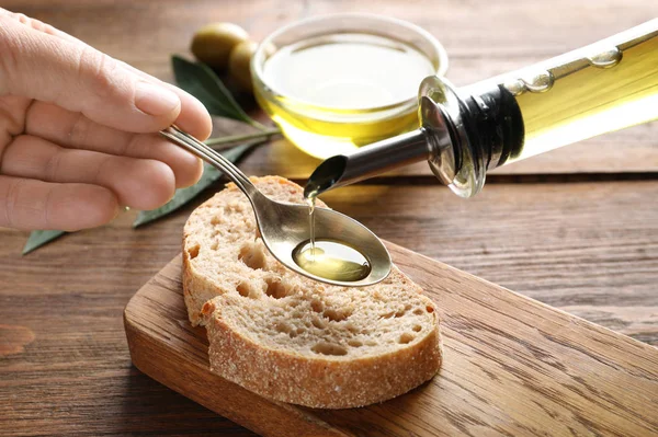 クローズ アップのテーブルでパンの上のスプーンに新鮮なオリーブ オイルを注ぐ男 — ストック写真
